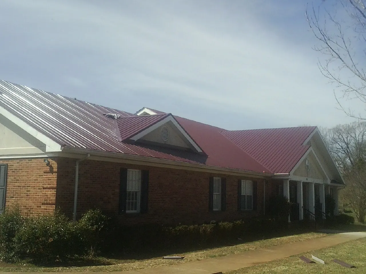 Red metal roof with gabled entries on a long brick building, from a Hail Damage Roof Repair job in Sausalito